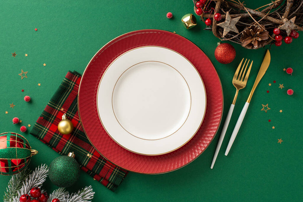 Karácsonyi ünnepi asztalterítés. Felsőrész edények, aranyozott evőeszközök, kockás szalvéta, baubles, természetes koszorú, csillag alakú konfetti, jeges fenyő ágak, fagyöngy, zöld háttér, szöveges terület - Fotó, kép