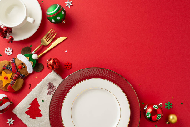 Organize inviting New Year's dinner table scene. Top view of dishes, gold utensils in charming pocket, napkin, mug, baubles, snowflakes on crimson backdrop with open space for text or advertisement - Photo, Image