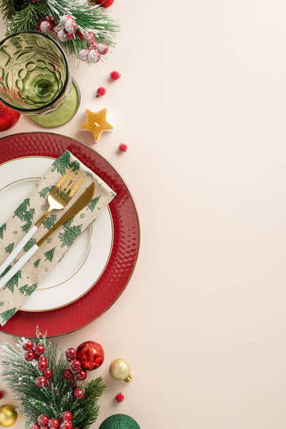 Design festive New Year's dining setup. Vertical top view of plates, gold cutlery, napkin, wine glass, baubles, candle, frosty fir twigs, mistletoe berries on gentle beige backdrop with space for text - Photo, Image