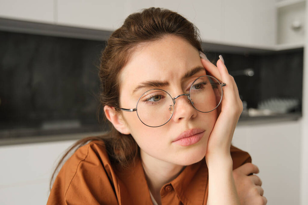 Porträt einer Frau, die über etwas Besorgniserregendes nachdenkt, Brille trägt, Kopf berührt, beunruhigt zu Hause sitzt. - Foto, Bild