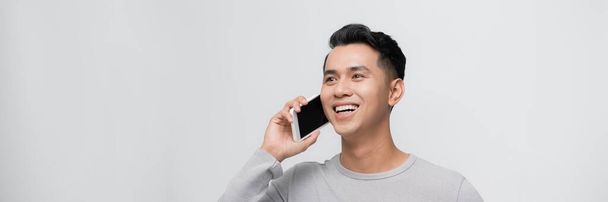 Hombre joven guapo hablando en el teléfono inteligente sobre fondo gris. - Foto, Imagen