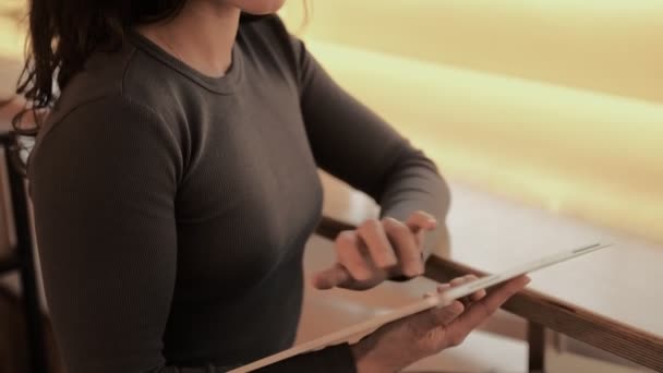 Jovencita guapa trabajando en la tableta digital mientras escribe en la pantalla, sentada en el café. Estilo de vida, gente, concepto de tecnología. Movimiento lento - Metraje, vídeo