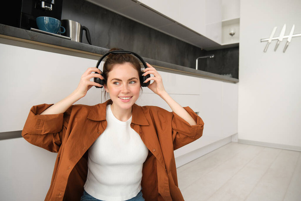 ケアフリーの女性は自宅で音楽を聴き,床に座り,ワイヤレスヘッドフォンを置き,笑顔で幸せに見えます. - 写真・画像