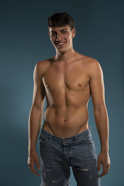 Молодой улыбчивый спортсмен. концепция: мужской организм после физических упражнений и диеты. мужское здоровье. Синий студийный фон - Фото, изображение