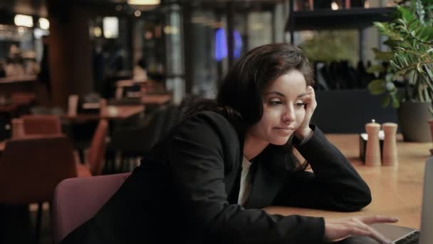 Schläfrige junge Frau gähnt, sitzt im Café, während sie auf dem Laptop tippt, auf den Tisch gestützt. Lifestyle, Business, Technologiekonzept. Zeitlupe - Filmmaterial, Video