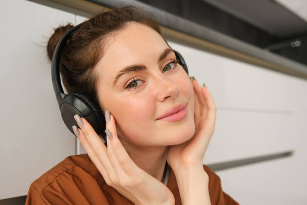 Πορτρέτο της χαμογελαστής γυναίκας με ακουστικά, ακούει μουσική, κοιτάζει την κάμερα. - Φωτογραφία, εικόνα