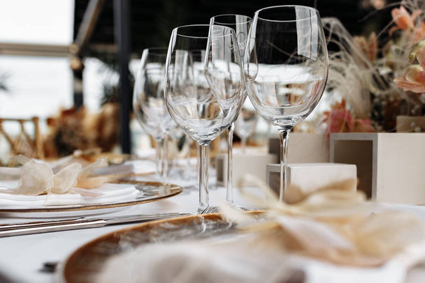Verres à vin transparents sur nappe blanche avec assiettes et couverts. Restaurant de luxe vue rapprochée dans des tons or coûteux. - Photo, image