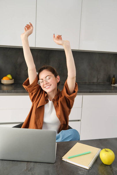 Portrait of cheerful young woman, student stretches her hands with pleased face, accomplish goal, finish working on project, using laptop and smiling pleased. - Photo, Image