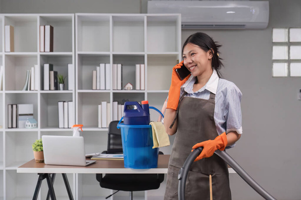 Asyalı bir ev hanımı işvereniyle iletişim kurmak için telefon kullanır. Ofisi temizlerken.. - Fotoğraf, Görsel