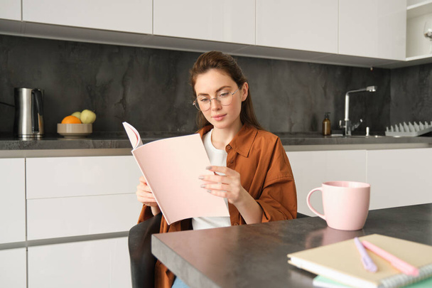 Portrait of woman working from home, sitting in kitchen with documents, opens folder, drinks tea. - Zdjęcie, obraz