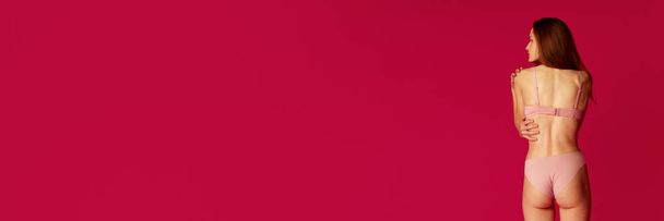 Bannière. Vue arrière de la fille vêtue de pyjama posant sur fond de studio rouge. Modèle joyeux ont la forme parfaite du corps, les fesses, le dos sain. Concept de beauté naturelle, jeunesse, mode, vente. Publicité - Photo, image