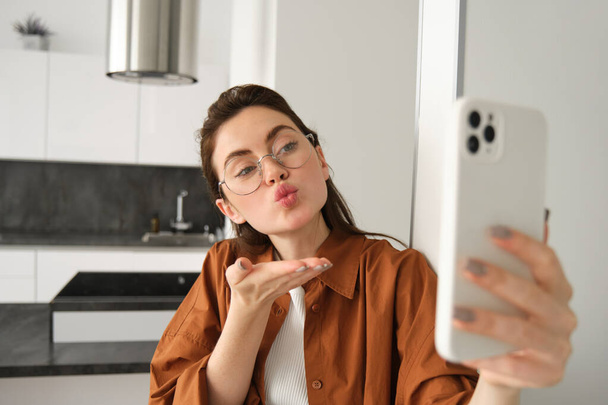 Πορτρέτο της κομψής όμορφη γυναίκα στο σπίτι, συνομιλίες βίντεο στο smartphone, συνδέεται με online συνάντηση από το σαλόνι της, lifestyle blogger κοινωνικών μέσων μαζικής ενημέρωσης καταγράφει ένα βίντεο στο κινητό τηλέφωνο. - Φωτογραφία, εικόνα