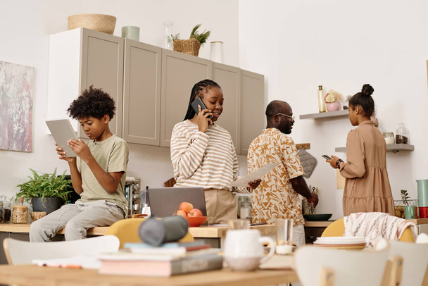 Mosolygó fekete nő hívja munkatársát, amikor a fia csinál házi feladatot, lánya és férje főzés ebéd - Fotó, kép