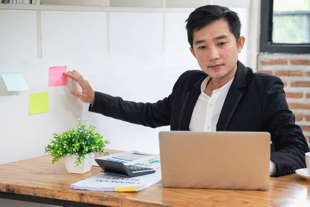 Serious businessman managing project tasks on sticky notes writes start-up business ideas using colorful Post-it stickers, plans corporate strategy board. Creative priority to-do list concept. - Photo, Image