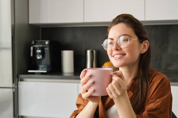 Beautiful young woman, drinking coffee, smiling and looking away with dreamy face, enjoying nice flavour and aroma. - Photo, Image