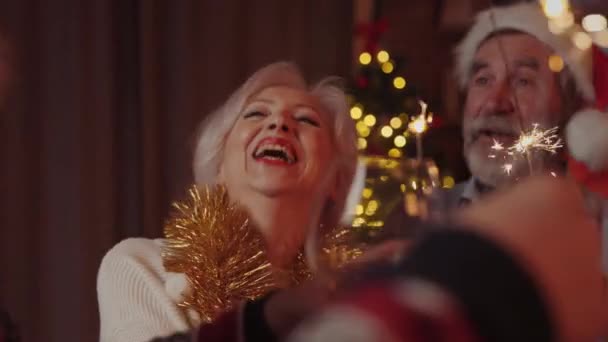 Nahaufnahme der Seniorin beim Tanzen, lächelnd auf der Silvesterparty mit ihren Freunden, die bei der Weihnachtsfeier Wunderkerzen in den Händen halten. Tanzen und Lachen. Festliche Stimmung - Filmmaterial, Video