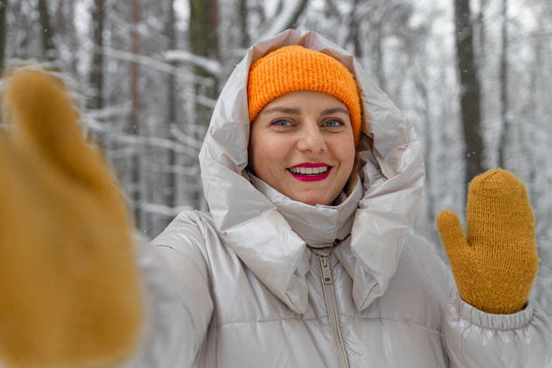 Fiatal női turista meleg ruhában és sárga kesztyűben szelfit készít, téli város, túrázás a hegyi erdőben. Sikeres kiránduló mosolyog a kamerába  - Fotó, kép