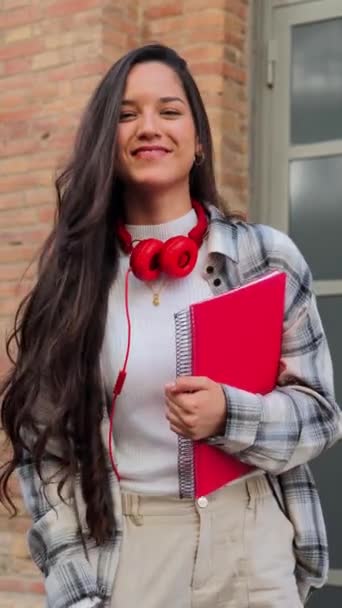 Függőleges egyéni portré egy csinos spanyol diáklányról, aki mosolyog és kamerába néz a középiskolában. Egy latin tinédzser lány képe, aki kint áll az egyetem területén. Oktatás - Felvétel, videó