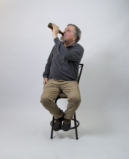 瓶からビールを飲みながら椅子に座っている老人 - 写真・画像
