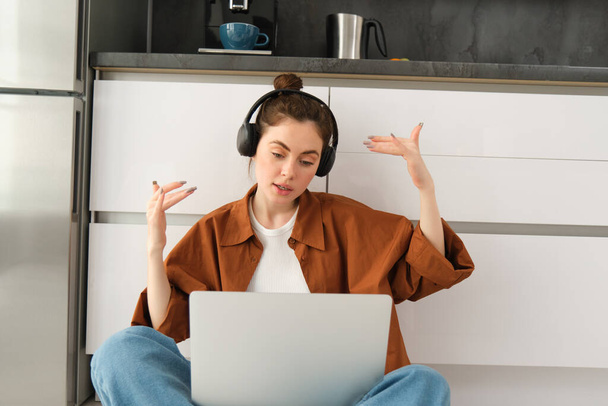 Excited young woman, programmer achieves goal, triumphing, winning on laptop, sitting in headphones, dancing with hands, celebrating victory. - Photo, Image