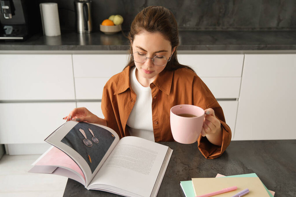 Enseñanza a distancia. Mujer joven en casa, estudiante estudiando en casa y tomando té, leyendo su libro de trabajo, revisando para el examen. - Foto, imagen