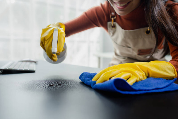Cleaning desk surface in office with sanitizer spray, wear gloves and wipe the table with a towel, the housekeeper is cleaning the work desk for hygiene because of the Covid-19, cleaning idea. - Photo, Image