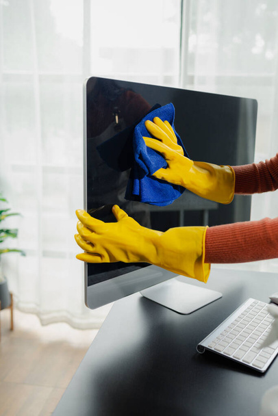 Ο επιστάτης καθαρίζει το γραφείο, καθαρίζει την οθόνη με ένα πανί, φοράει γάντια και σκουπίζει με μια πετσέτα, φορά γάντια από καουτσούκ κατά την εργασία με χημικές ουσίες καθαρισμού, ιδέα καθαρισμού. - Φωτογραφία, εικόνα