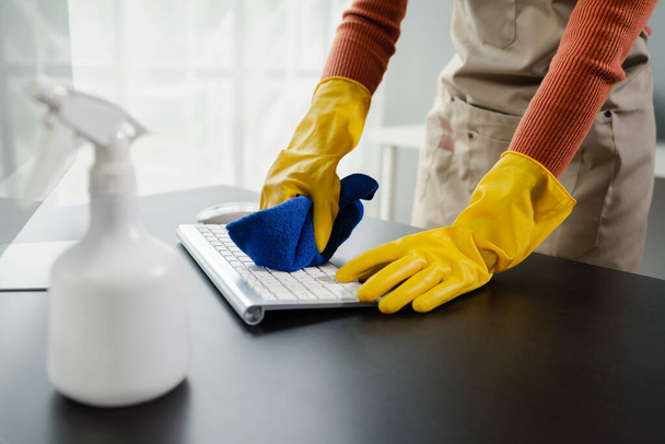 Sprzątacze wycierający sprzęt biurowy, wyczyścić klawiaturę ręcznikiem i środkiem dezynfekującym, nosić gumowe rękawice podczas pracy z chemikaliami czyszczącymi, pomysł na czyszczenie. - Zdjęcie, obraz