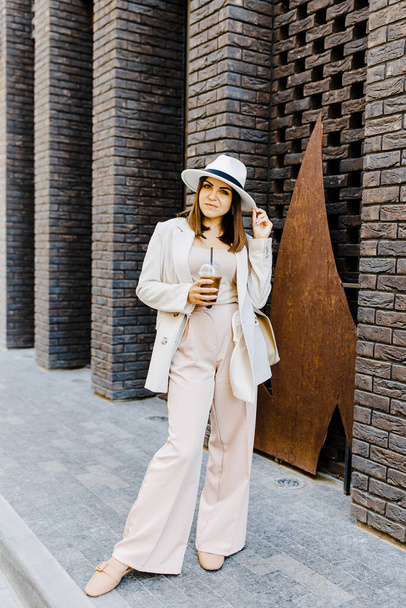 Beautiful woman going to meeting with cold coffee walking on the street. Portrait of successful business woman holding cup of cold drink in hand on her way to work on city street - Фото, изображение