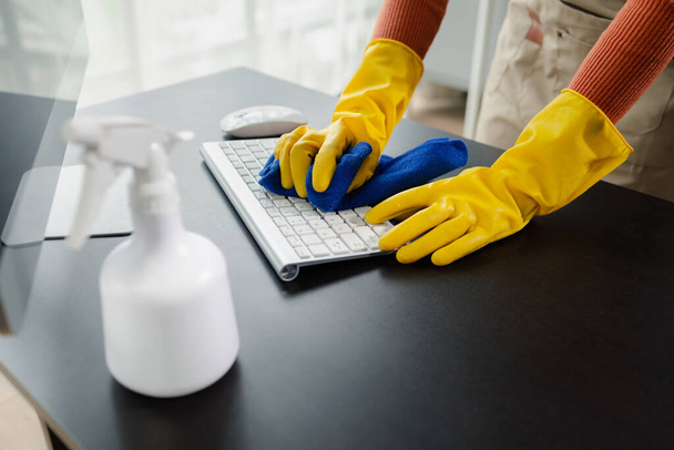 Ofis ekipmanlarını temizleme, klavyeyi havlu ve dezenfektanla silme, temizlik kimyasallarıyla çalışırken lastik eldiven giyme, temizlik fikri.. - Fotoğraf, Görsel