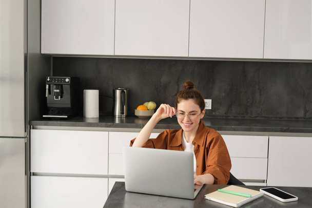 Retrato de mujer freelancer, programadora trabajando desde casa. Estudiante o propietaria de un negocio sentada con portátil en cocina. - Foto, imagen