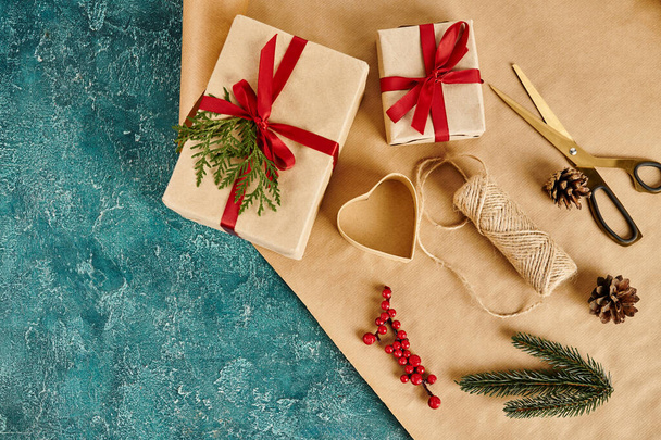 подарочные коробки и сосновый декор с ягодами падуба рядом с ножницами и бумагой ремесла на голубом фоне - Фото, изображение