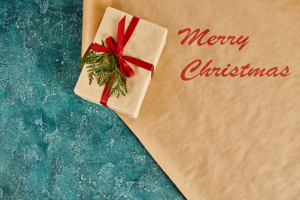 decorated gift box on craft paper with Merry Christmas inscription on blue textured backdrop - Photo, Image