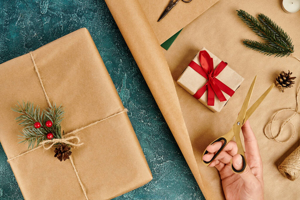 vue recadrée de la femme avec des ciseaux près des boîtes cadeaux fournitures de décoration de Noël sur texture bleue - Photo, image