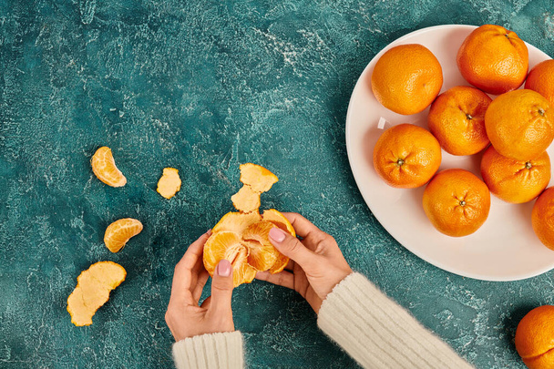 cropped view of woman peeling fresh and sweet tangerine on blue textured backdrop, Christmas concept - Photo, Image