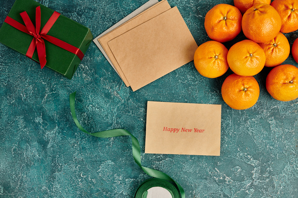obálka s šťastný nový rok v blízkosti pozdravu u mandarinek a dárkové krabice s stuhou na modrém pozadí - Fotografie, Obrázek
