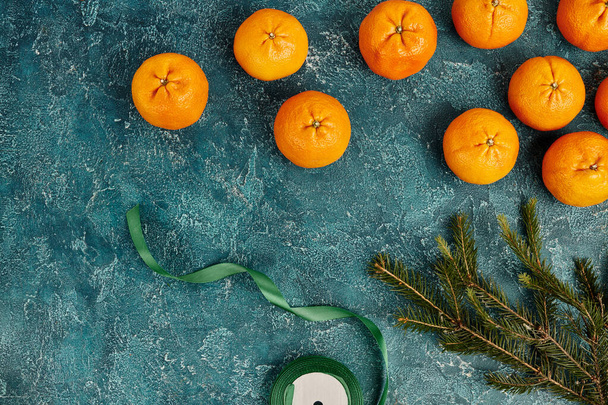 tuoreet mandariinit männyn oksan vieressä ja koristeellinen nauha sinisellä kuvioidulla taustalla, joulu - Valokuva, kuva