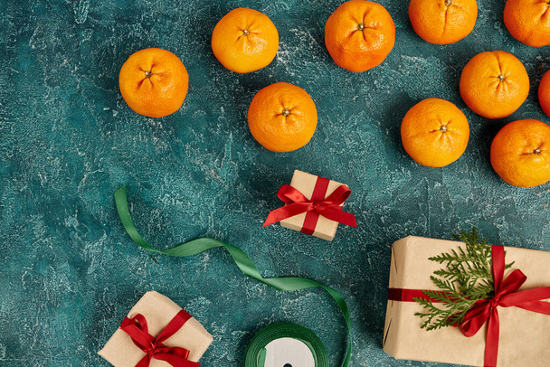 спелые мандарины и украшенные подарочные коробки рядом с лентой на голубой текстурированной поверхности, рождественская тема - Фото, изображение