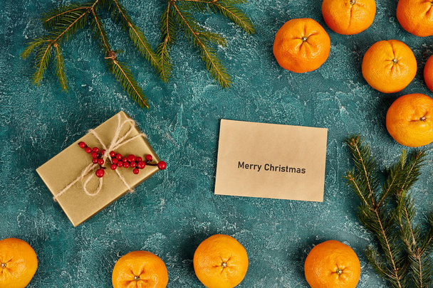 enveloppe met vrolijke kerstbelettering in de buurt van mandarijnen en geschenkdoos met hulst bessen, Kerstmis - Foto, afbeelding
