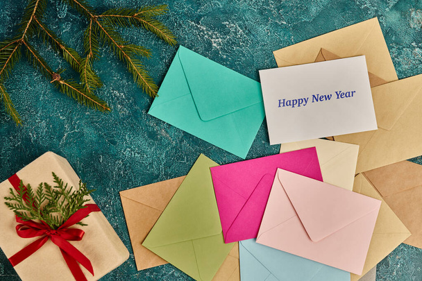 красочные конверты и подарочная коробка рядом сосновые ветви на голубой деревенской поверхности, с Новым годом надписи - Фото, изображение
