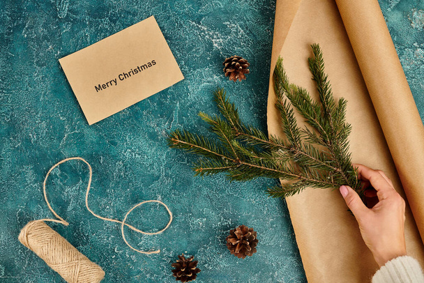 cropped view of woman with pine branch near envelope with Merry Christmas lettering and diy supplies - Photo, Image