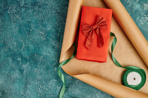 geschenkdoos met rood lint op ambachtelijk papier in de buurt van decoratief lint op blauwe textuur achtergrond, Kerstmis - Foto, afbeelding