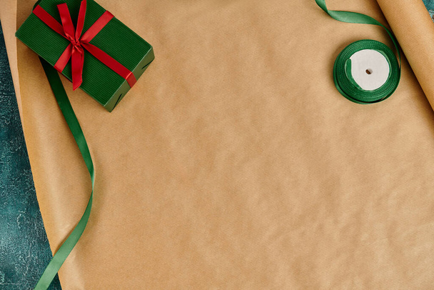 diy kerstcadeau, groene geschenkdoos met rode strik bij decoratief lint op ambachtelijk inpakpapier - Foto, afbeelding