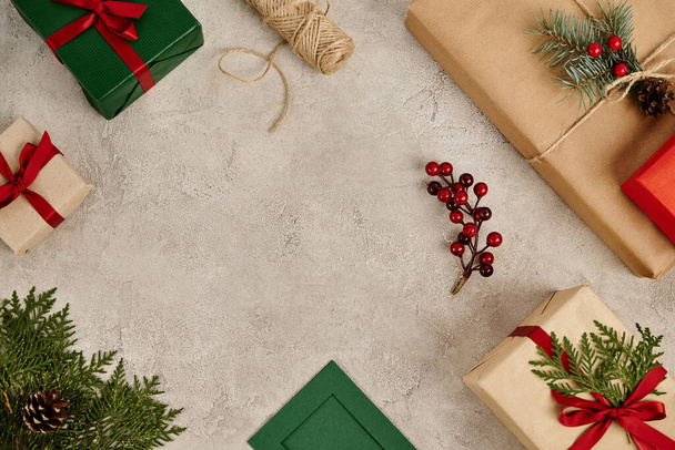подарки с красными лентами и сосновыми ветвями с ягодами падуба на сером текстурированном фоне, Рождество - Фото, изображение