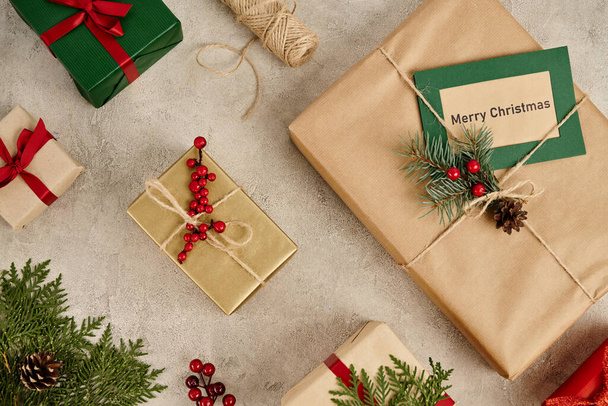 Şenlikli arka plan, Mutlu Noeller tebrik kartı içinde çam dalları ve kutsal çilekler olan hediye kutularının yanında. - Fotoğraf, Görsel