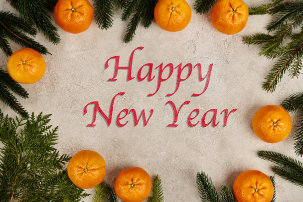 šťastný novoroční nápis v rámu mandarinek s borovicovými a jalovcovými větvemi na šedé textuře - Fotografie, Obrázek