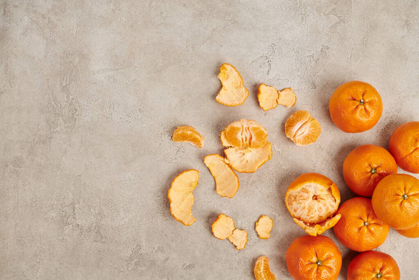 top view of whole and peeled ripe mandarins on grey textured backdrop, Christmas concept - Photo, Image