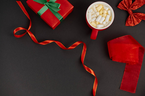 kubek gorącej czekolady z pianką w pobliżu prezentów świątecznych i błyszczący łuk z wstążkami na czarno - Zdjęcie, obraz