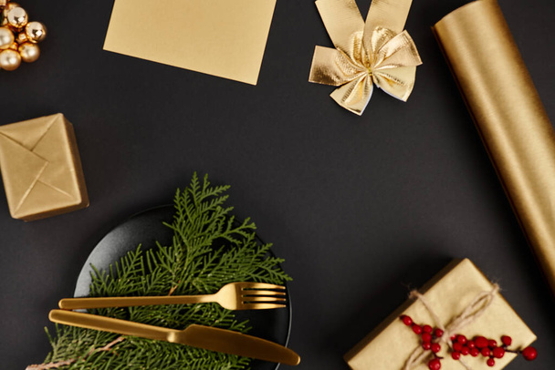 золотые столовые приборы на можжевеловых ветках возле блестящего рождественского декора на черном фоне, эксклюзивность - Фото, изображение