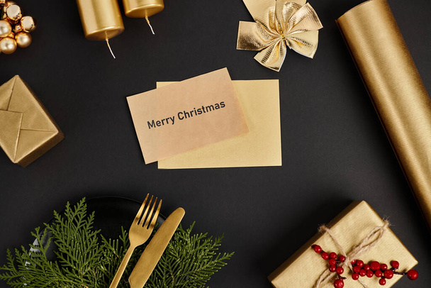 cartão de saudação brilhante com letras Feliz Natal perto de talheres dourados e decoração festiva em preto - Foto, Imagem